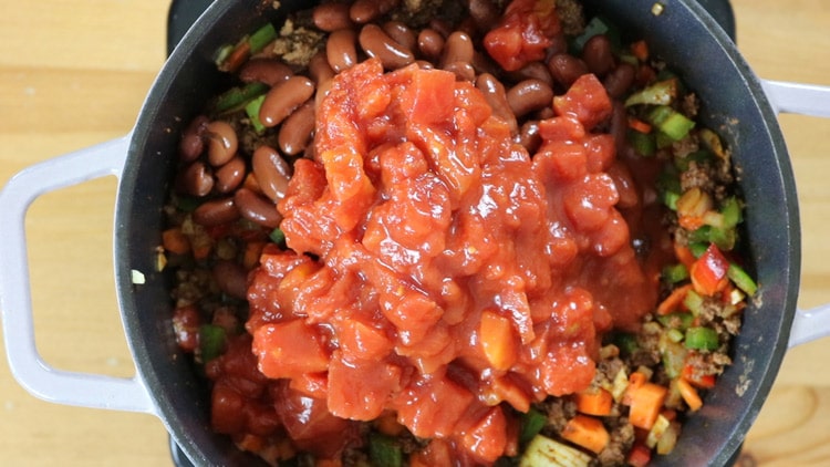 Then, add beans, tomatoes, tomato sauce and keep stirring to prevent the meat from sticking to the bottom.This will create layers of flavor in the dish. add-the-beans,-tomatoes-and-tomato-paste